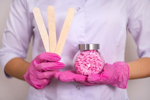 a sugaring master in white clothes and pink gloves holds chopsticks a jar with wax granules for the procedure
