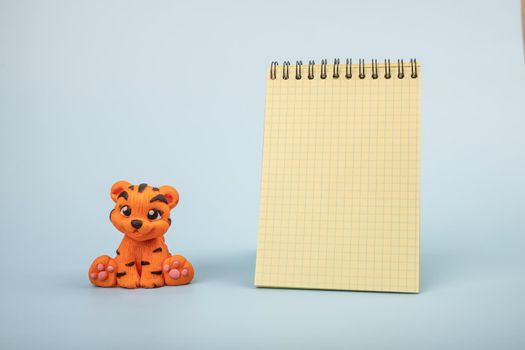 A hand-sculpted orange tiger figurine on a blue background with a notepad for notes. The year 2022 is the year of the tiger according to the Eastern calendar.