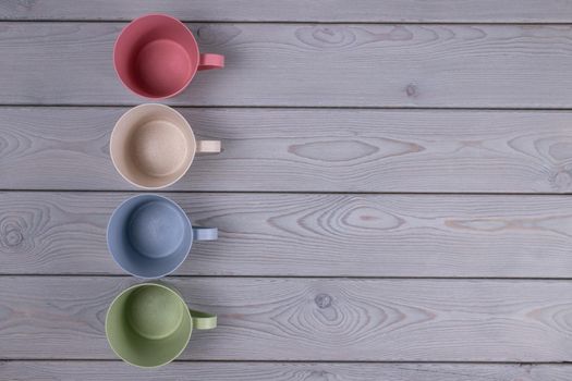 Top view of empty multicolored mugs made of ecological material on a gray wooden table. Copy space