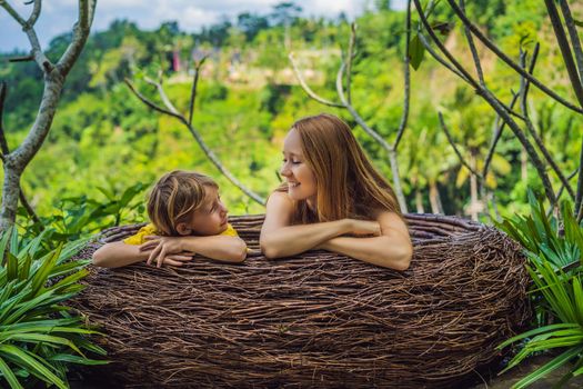 Bali trend, straw nests everywhere. Happy family enjoying their travel around Bali island, Indonesia. Making a stop on a beautiful hill. Photo in a straw nest, natural environment. Lifestyle. Traveling with kids concept. What to do with children. Child friendly place.