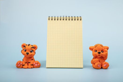 Two handmade orange tiger figurines on a blue background with a notepad for notes and notes. The year 2022 is the new year of the tiger according to the Eastern calendar.