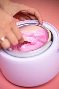 Wax in a heating container. A cosmetologist who uses hot wax for depilation and prepares it in a special device