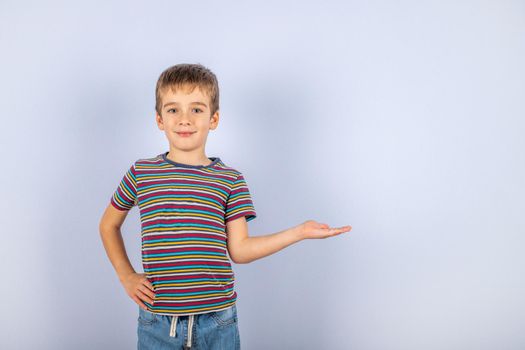 A beautiful young boy on a blue background smiles, shows and points to something on a blue background with a place to copy