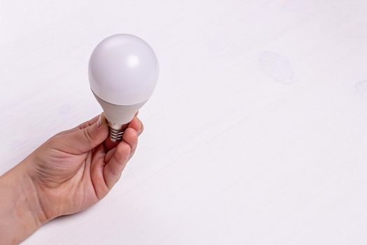 A child's hand holds an LED light bulb on the background of a light wooden table