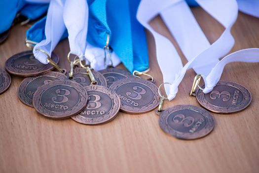 A bunch of bronze medals on a white and blue ribbon for third place in sports competitions. Medals on a wooden table.