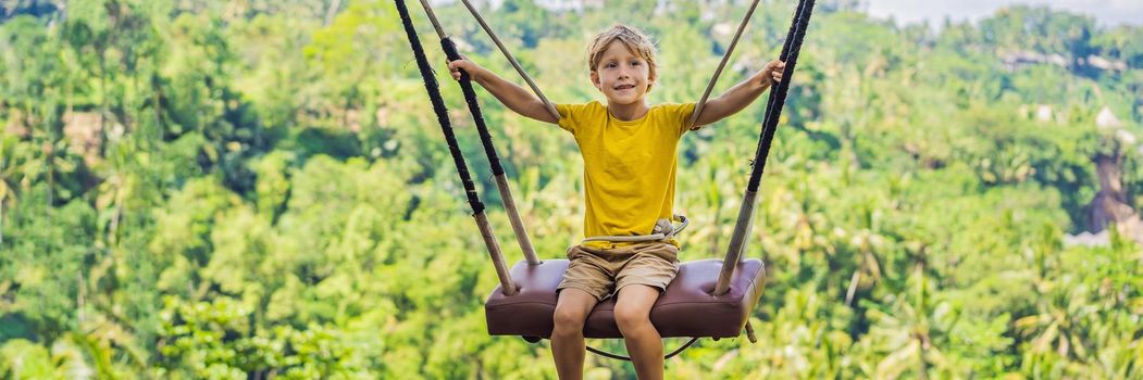 BANNER, LONG FORMAT Young boy swinging in the jungle rainforest of Bali island, Indonesia. Swing in the tropics. Swings - trend of Bali. Traveling with kids concept. What to do with children. Child friendly place.