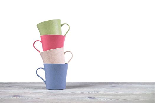 A stack of four ecological mugs on a wooden table on a white background. Dishes made of eco-plastic.