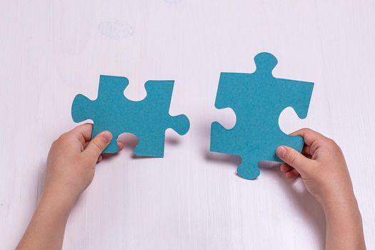 Children's hands hold two puzzle pieces on a light wooden background.