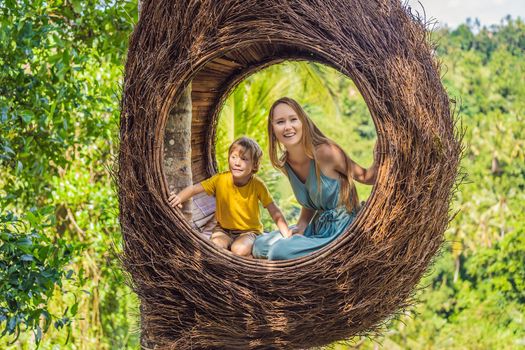 Bali trend, straw nests everywhere. Happy family enjoying their travel around Bali island, Indonesia. Making a stop on a beautiful hill. Photo in a straw nest, natural environment. Lifestyle. Traveling with kids concept. What to do with children. Child friendly place.