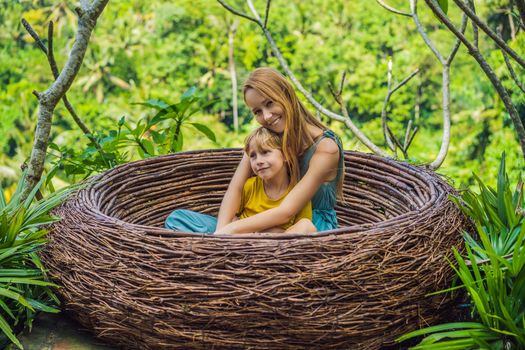 Bali trend, straw nests everywhere. Happy family enjoying their travel around Bali island, Indonesia. Making a stop on a beautiful hill. Photo in a straw nest, natural environment. Lifestyle. Traveling with kids concept. What to do with children. Child friendly place.