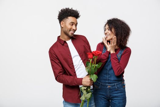 Beautiful elegant couple is hugging and smiling, on gray background. Girl is holding roses.