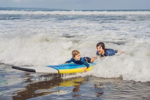 Father or instructor teaching his 5 year old son how to surf in the sea on vacation or holiday. Travel and sports with children concept. Surfing lesson for kids.