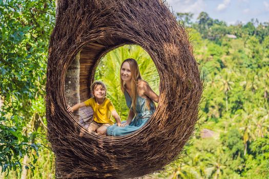 Bali trend, straw nests everywhere. Happy family enjoying their travel around Bali island, Indonesia. Making a stop on a beautiful hill. Photo in a straw nest, natural environment. Lifestyle. Traveling with kids concept. What to do with children. Child friendly place.