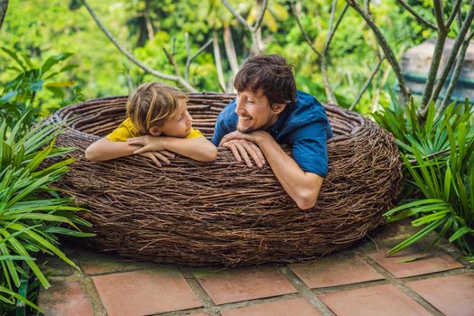 Bali trend, straw nests everywhere. Child friendly place. Happy family enjoying their travel around Bali island, Indonesia. Making a stop on a beautiful hill. Photo in a straw nest, natural environment. Lifestyle. Traveling with kids concept. What to do with children.