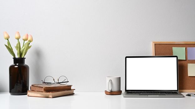 Contemporary workplace with laptop computer, coffee cup, flower pot and stationery on white table.