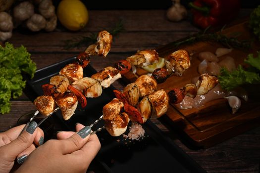 Close up vie woman hand holding delicious barbecue skewers with grilled chicken, cherry tomato, sweet pepper and onions.