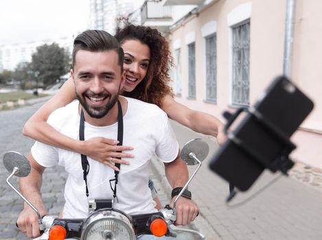 Happy couple on scooter making selfie photo on smartphone outdoor