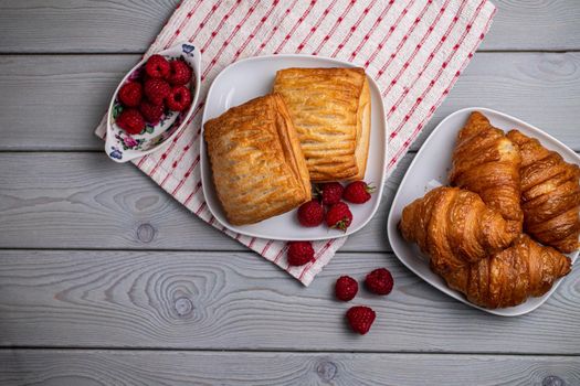 Delicious fresh croissants and sweet raspberry puffs on a wooden table.