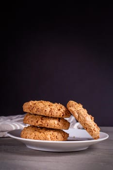 A stack of oatmeal cookies in a saucer and a napkin on a wooden table on a dark background.