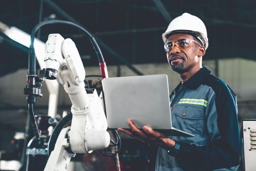 African American factory worker working with adept robotic arm in a workshop . Industry robot programming software for automated manufacturing technology .