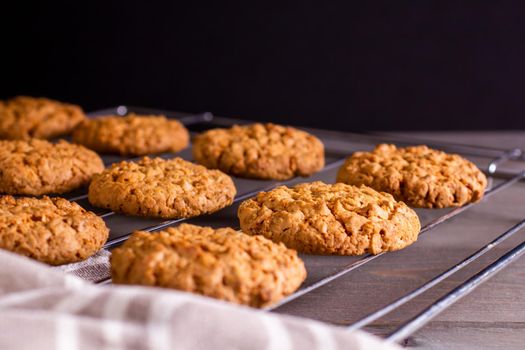 Freshly baked warm oatmeal cookies with towel on cooling rack on dark background