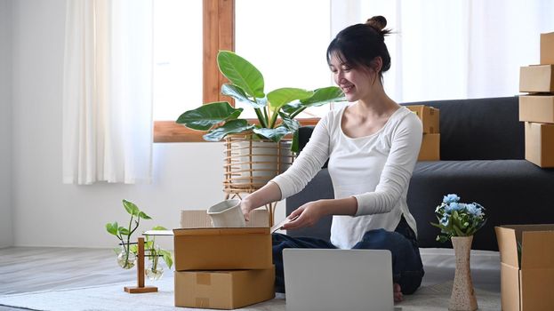 Young woman small business entrepreneur packing product in cardboard box for delivery to customers. Online selling, e-commerce.