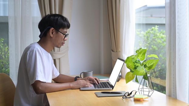 Side view focused asian man freelancer working online, reading email on computer laptop at home.