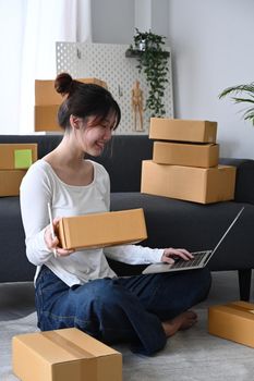 Smiling female online seller answering customers through laptops computer. Online selling, e-commerce concept.