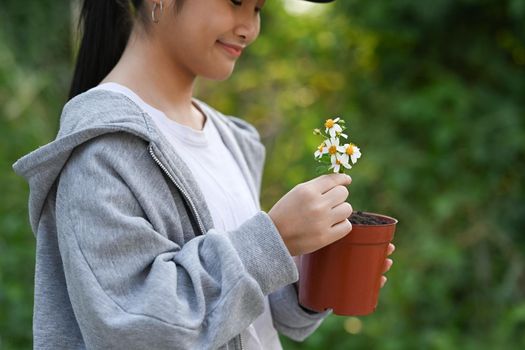 Cute asian girl holding potted plant in hands against blurred green nature background. Earth day, Ecology concept.