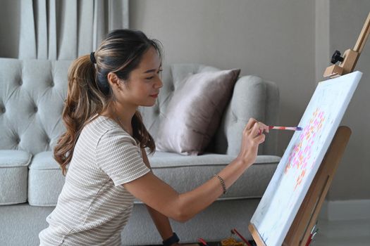 Peaceful young woman painting picture on canvas with watercolor.