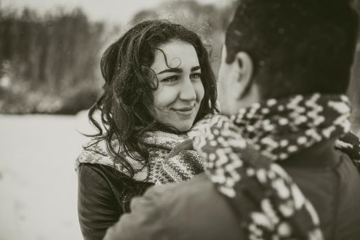 young man and woman stand kissing and hugging. bride and groom in love couple in knitted scarf and mittens in winter with snow and snowflakes. wedding dress. mexican people