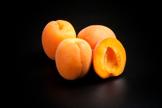 Three whole apricots and one cut in half on a black background