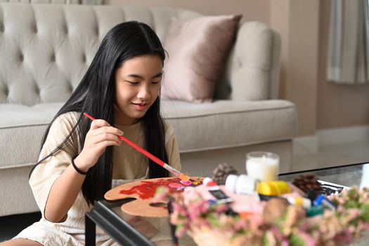 Elementary girl spending leisure time at home and painting with watercolors.