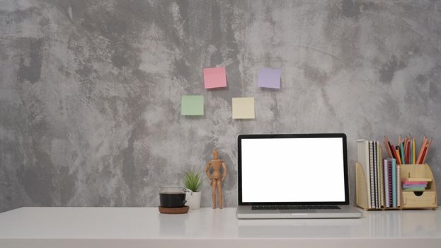 Front view laptop computer with blank screen, coffee cup and supplies on white table against concrete wall.