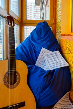A glazed golden-orange balcony in a winter city, a place to relax with a blue paint bag, guitar and sheet music. The concept of music, relaxation and hobbies