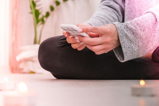 Young millennial blonde woman doing yoga exercise watching tutorial lesson on mobile phone stretching fitness at balcony home. Mindfulness meditation. The concept of online training. Video lessons. Self-isolation is beneficial. Exercise for Lose weight, increase flexibility And tighten the shape. Young slim athletic girl practices yoga at home in online lessons.