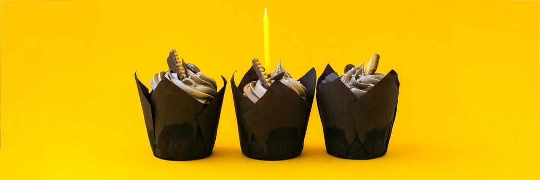 Delicious chocolate cupcakes with cream and candle on yellow background. Three chocolate muffin. Birthday cake party. Homemade Chocolate Cupcake