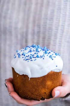 The cook Hands hold Easter cake with white topping and blue sprinkles. Woman holding traditional Russian Easter cake. Homemade pie for spring holiday celebration