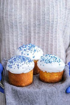 The cook Hands hold Easter cake with white topping and blue sprinkles. Woman holding traditional Russian Easter cake. Homemade pie for spring holiday celebration