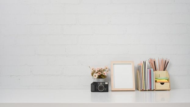 Creative workplace with camera, coffee cup, picture frame and stationery on white table.