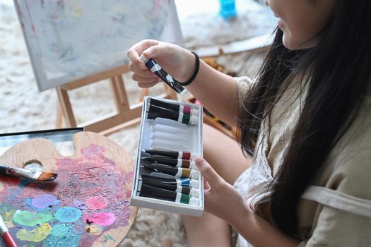 Cropped shot girl hand choosing acrylic paint tube for her artwork.