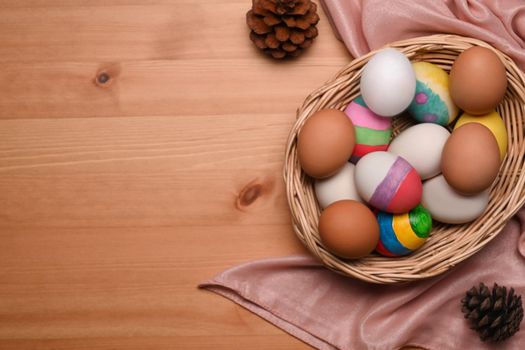 Wicker basket filled with painted Easter eggs over wooden background.