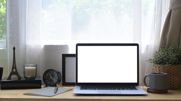 Front view laptop computer with white screen, potted plant, coffee cup and picture frame on wooden table.