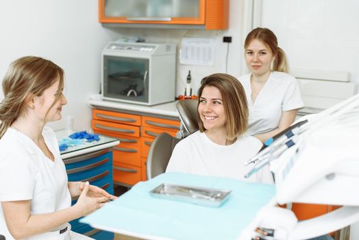 Medical dentist team talking with patient woman talking at dental clinic office preparing for treatment. Female dentist and her assistant in dental office talking with female patient.