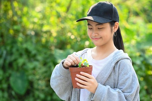 Asian girl holding young plant against sunshine and green nature background. Saving the world, earth day concept.