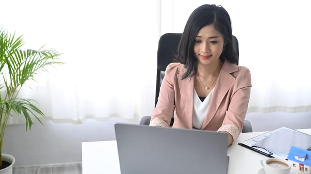 Young woman sitting in bright modern office and using laptop computer.