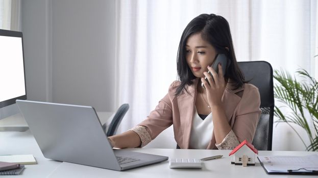 Busy female entrepreneur sitting in front of laptop computer and talking on mobile phone.