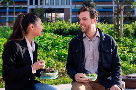 coworkers chatting and eating a salad during a work break in the park next to the office, concept of healthy fast food at work