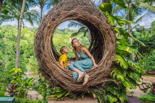 Bali trend, straw nests everywhere. Happy family enjoying their travel around Bali island, Indonesia. Making a stop on a beautiful hill. Photo in a straw nest, natural environment. Lifestyle. Traveling with kids concept. What to do with children. Child friendly place.