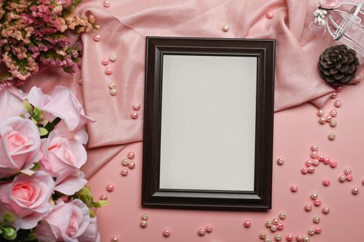 Empty frame, pink roses and dry flowers on pink background.